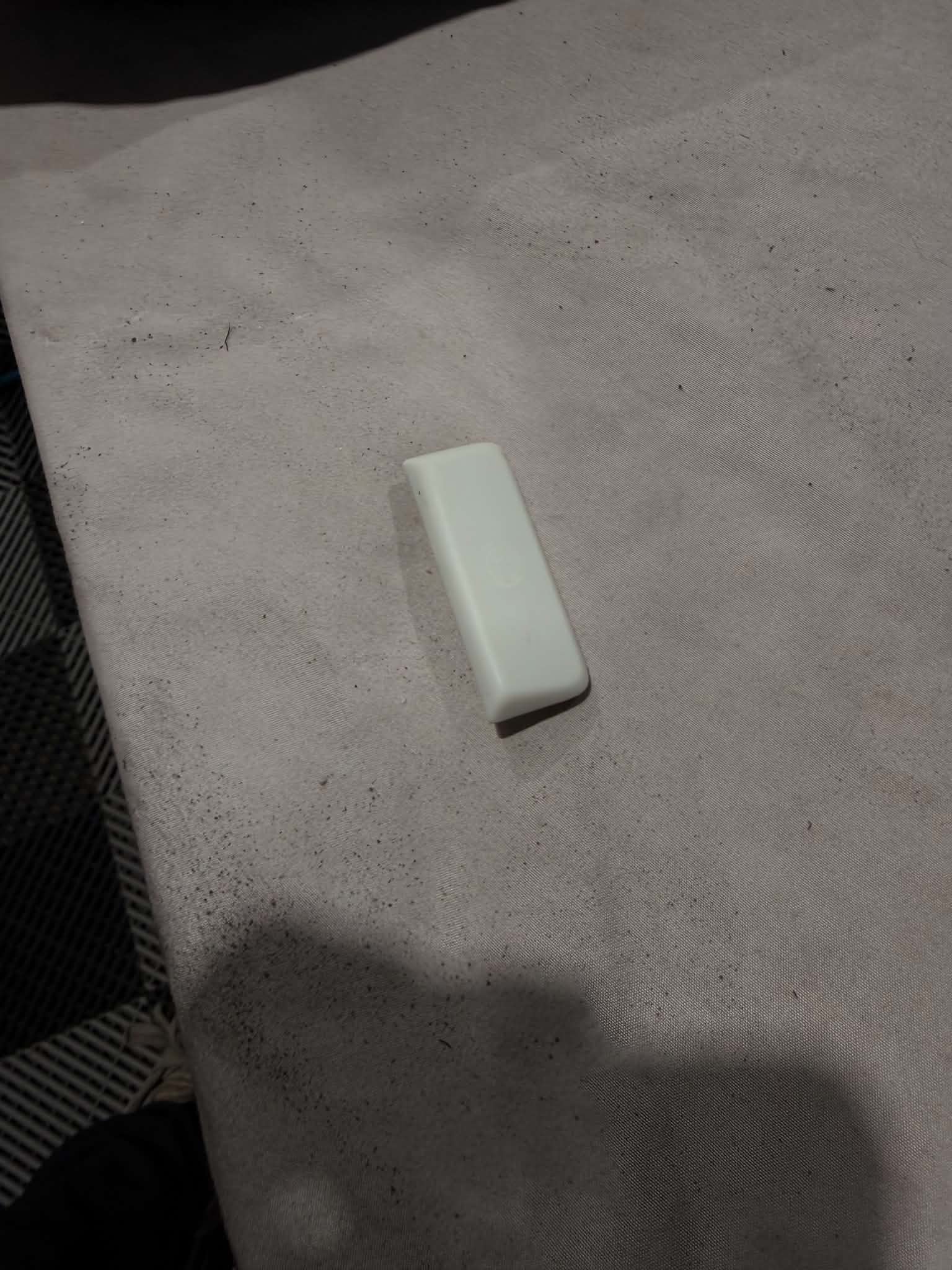 The same park brake button fully stripped back to bare white plastic with every trace of the failed coating removed, ready for recoating and laser etching